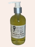 A bottle of Oegonia SoapWorks Witch's Wash glycerin hand wash with a glass pump and silver collar, containing a gold liquid blycering soap, set against a plain light background.